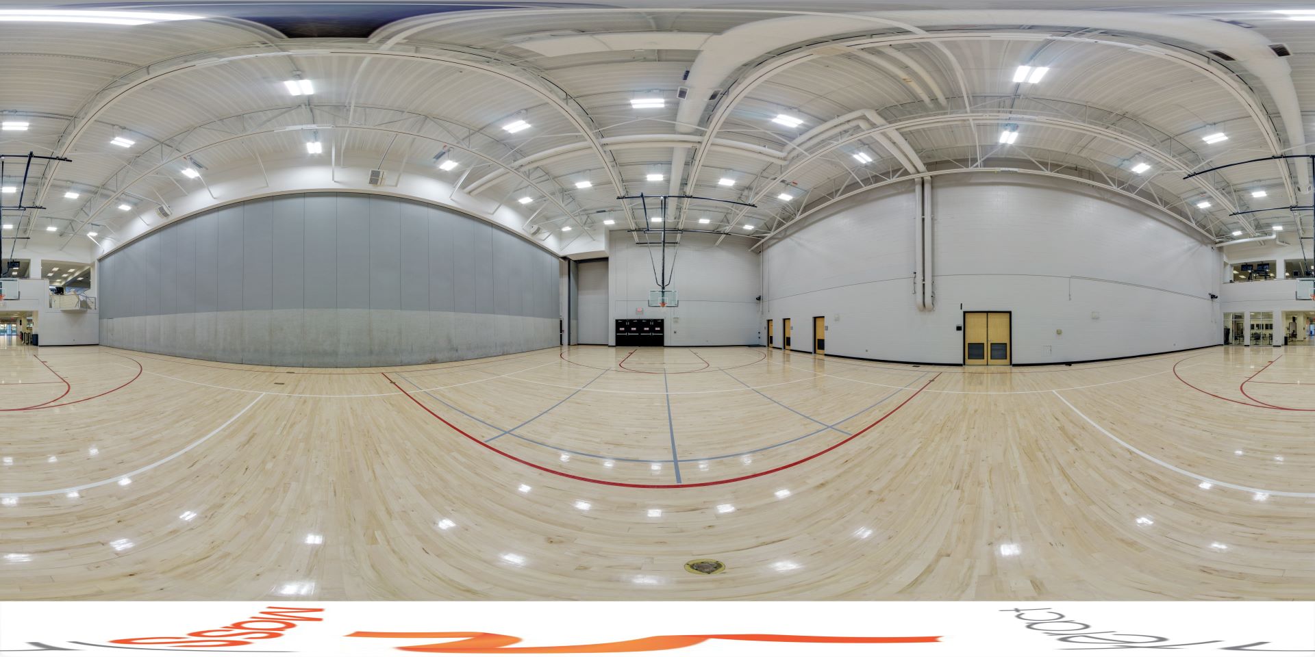 A panoramic view of the intramural gym at Florida Tech, featuring a spacious wooden floor with red and white court lines, high ceilings with lighting, and basketball hoops on either end